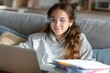 © maria_lh - Teenage girl with glasses and earphones studying on laptop at home. Student watching online lesson. Distance learning concept
