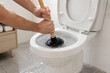 © Svitlana Ozirna - Hands using plunger to unclog overflowing toilet in bathroom emergency