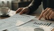 © hathairat - Person Reviewing Printed Reports and Graphs in Office Setting
