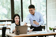 © Witoon - Smiling business colleagues collaborating at a modern office, reviewing work on a laptop while sharing ideas over coffee, highlighting teamwork, productivity, and professional communication.