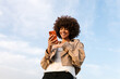 © Ezequiel Gimenez/Stocksy - Young woman smiling using smartphone outdoors