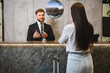 © Serhii - Happy male concierge talking visiting woman at reception desk