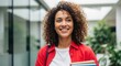 © Hungarian - Happy young woman with curly hair holding books on a modern university campus, smiling student portrait.