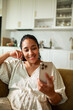 © Marko Geber - Smiling woman using smartphone on couch in home kitchen