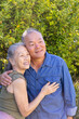 © wavebreak3 - Senior Asian couple standing in backyard, wearing olive green top and denim shirt, embracing