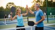 © soem - A senior couple celebrates a pickleball victory. A man and a woman are standing behind the net, holding pickleball paddles and giving each other a high five.