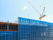 © pirom - Construction building crane scaffolding blue safety urban architecture development site. Construction site with blue safety netting scaffolding and large crane clear sky showcasing urban