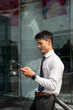 © bongkarn - Asian businessman office worker looking or using smartphone outside glass facade of company building