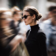 © JPbodyparts - Elegante Frau mit Sonnenbrille inmitten einer verschwommenen Menschenmenge. Ausdrucksstarkes Lifestyle-Motiv zu Großstadt, Hektik, Fokus, Individualität, Business und urbanem Leben.