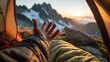 © dika - A hand reaches toward a sunrise vista over alpine peaks from within a tent. Golden light bathes the scene