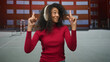 © Krakenimages.com - Teenage woman wearing headphones pointing both index fingers upward in a gymnasium with a red sweater; playful joy.