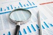 © mrzn - Close up view of magnifying glass over financial spreadsheet and bar charts for detailed business data inspection with analysis