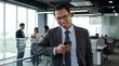 © Hariyanto Bromantio - Indonesian Business Executive Checks a Critical Smartphone Update While Walking Through a Modern Office Corridor, Coordinating Project Tasks and Next Steps as a Nearby Team Reviews Performance