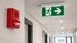 © Jafree - Exit sign with green indicator above fire alarm strobe in office hallway. Emergency evacuation protocol and safety equipment in public building. Regulation for fire prevention and security