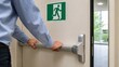 © Jafree - Man opening emergency exit door with panic bar in office building. Sign indicating evacuation route for fire safety and industrial compliance. Concept of escape in workplace emergency situation