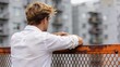 © Wei - Young man standing on balcony looking at city buildings, urban lifestyle background, contemplative mood, residential architecture view