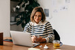 © (JLco) Julia Amaral - At her desk, the woman balances smartphone tasks with laptop work in a home office