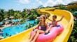 © ImageNation - Excited children riding a yellow water slide with a pink inflatable tube at a sunny tropical resort water park on a summer vacation day filled with fun and laughter and splashing water