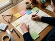 © ymamoto - Overhead view of person meticulously planning and drawing architectural blueprints with sticky notes for project management and inspiration