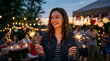 © Bilal - Young woman smiling while holding sparkling fireworks at outdoor evening celebration with string lights