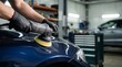 © Eve - Close up of technician hands polishing blue car fender with dual action orbital sander machine. Detailer worker buffering automobile body paint coating in modern garage service workshop.