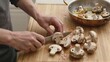 © joeycheung - Person slicing mushrooms on wooden board near copper pan with sauteed pieces.