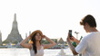 © blueringmedia - Young Man Taking Photo of Woman by Wat Arun in Bangkok