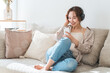 © buritora - A relaxed woman sitting on a sofa at home, listening to music with headphones on.