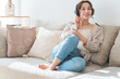 © buritora - A relaxed woman sitting on a sofa at home, listening to music with headphones on.