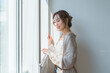 © buritora - A stylish woman standing by the living room window.