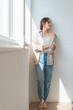 © buritora - A woman (model, fashion) standing by a window bathed in sunlight.