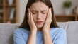 © Moopingz - A young woman sits on a couch, holding her head with both hands, experiencing a severe migraine.