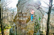 © anatoliy_gleb - Shirtless rock climber standing on sandstone formation after ascent, secured with rope, looking at camera, autumn forest and mountains background, outdoor adventure concept