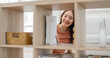 © Thitongpi - Asian woman shelf bookcase home smiling storage interior organization woman arranging item on wooden furniture in bright living room