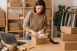 © inst - Young Business Woman Packing a Cardboard Box for Order Shipment in Her Small Online Shop Office