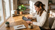 © kinkin - Young Woman Working on Digital Tablet with Stylus Sitting at Wooden Desk in Sunlit Home Office Workspace