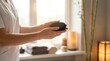 © Stitch - Spa therapist holding hot black massage stones near a window
