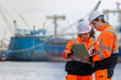 © JU.STOCKER - Logistics engineers using a laptop to coordinate operations at a shipping port, Port workers inspecting freight shipping, Team of marine logistics specialists managing shipping cargo at the harbor
