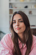 © Daniel - Young woman with long brown hair wearing a pink striped shirt, posing for a close-up portrait with a bookshelf in the blurred background, embodying quiet confidence and a relaxed indoor lifestyle