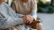 © Katerina Bond - A caregiver gently holds an elderly person's hands, offering comfort beside a framed family photograph.