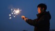 © Studicon - Young man holding a sparkler in the evening twilight during an outdoor celebration