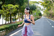 © Pavitra - Asian sportswoman wearing headphones while running exercise in garden.