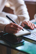 © Farknot Architect - Vertical closeup image of a woman writing on a notebook while working on laptop computer
