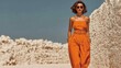 © 楠 刘 - Elegant African model walking in desert wearing burnt orange cropped top with waist belt, straight-leg pants, gold bracelet, sunglasses, high heels, stylish full-body fashion look