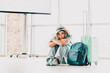 © deagreez - Sad woman in casual attire waiting at an airport terminal with suitcase and backpack depicting travel and leisure