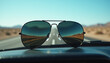 © ilkerinside - Macro of aviator sunglasses on a dashboard reflecting an empty desert highway.