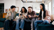 © DMegias - Happy young friends enjoying video games together, sitting on a sofa in a bright living room, having fun and bonding