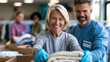 © Nataliya - Faceless diverse group of volunteers smiling while sorting folded clothes into donation boxes at bright community center with clothing racks visible, charitable giving concept,
