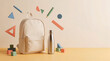 © Rendara Studio - Canvas backpack and water bottle with floating school supplies on a beige background