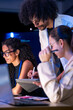 © ultramansk - Low-light scene where a diverse, multiethnic software team share a moment over the laptop in a modern technology office bathed in blue light, an image of teamwork and inclusion (frame 197)